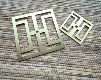May include: Two brass-colored, geometric square coasters with a cut-out design. The coasters have a repeating pattern of rectangles and squares, with a small hole in the center of each. The coasters are displayed on a textured, woven surface.