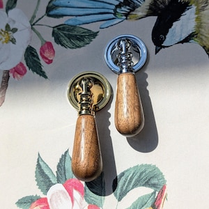 May include: Two cabinet pulls with wooden handles. One pull has a gold-toned base, the other has a silver-toned base. The pulls are set against a floral and bird-themed background.