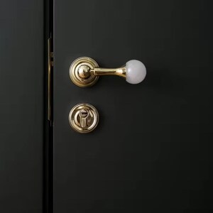 May include: A gold door handle with a white knob on a dark green door. The handle is a lever style with a round base. The door is closed.