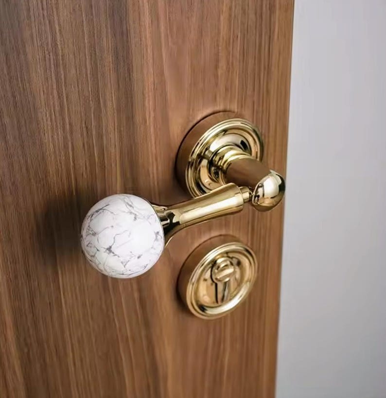 May include: A gold door handle with a white marble knob. The handle is mounted on a wooden door.