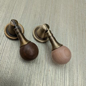 May include: Two cabinet pulls with a brass finish and wooden knobs. One knob is dark brown, the other is light brown. The pulls have a classic design, suitable for furniture restoration or new builds.