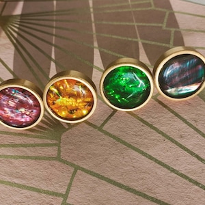May include: Four cabinet knobs with gold-toned rims and iridescent centres in red, orange, green, and blue. These decorative knobs are likely for furniture. Each knob has a diameter of approximately 2.5 cm.