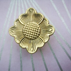 May include: A gold-coloured, flower-shaped cabinet knob. The knob has a detailed design with a textured centre and petal-like edges. The hardware is likely made of metal and is suitable for furniture or decorative projects.