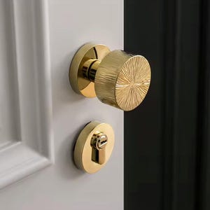May include: Gold door handle with a textured, circular knob and a separate keyhole cover. The handle is mounted on a white door.