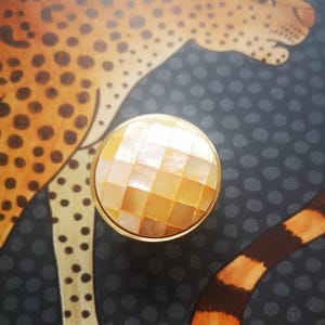 May include: A round cabinet knob with a gold rim and a mosaic surface of light-orange square tiles. The knob is set against a backdrop of a leopard illustration with orange and black spots.