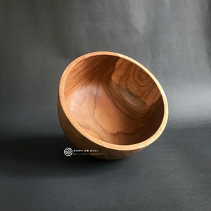 May include: A large, round, wooden bowl with a natural wood finish. The bowl is empty and is sitting on a dark gray surface.
