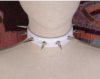 May include: White leather choker with silver spikes. The choker is on a white mannequin.