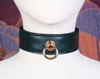 Könnte beinhalten: Ein dunkelgrünes Lederhalsband mit einem goldfarbenen Ring.