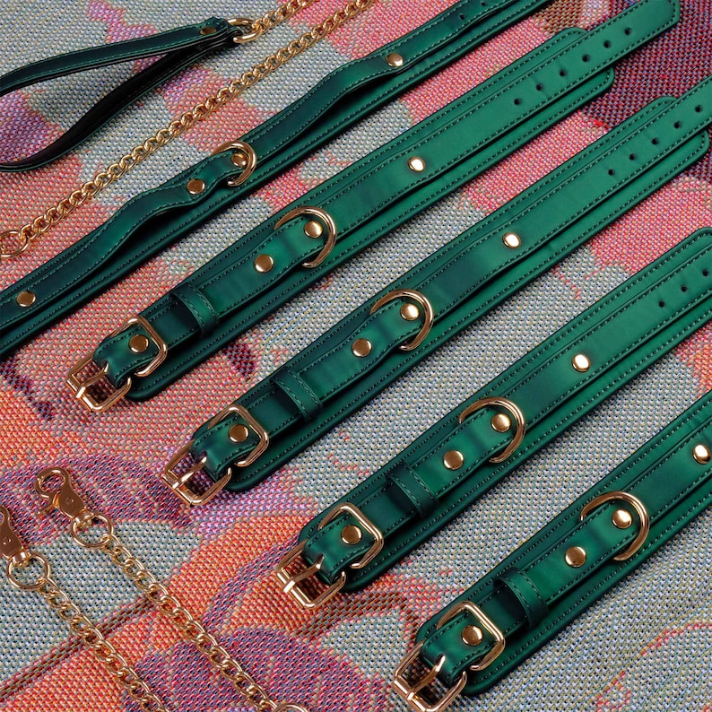 May include: Five green leather collars with gold metal hardware and a gold chain leash. The collars are different sizes and have a shiny finish.