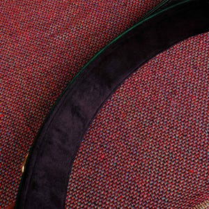 May include: A close-up of a black and green fabric hat with a black velvet band. The hat is on a red and green patterned fabric.