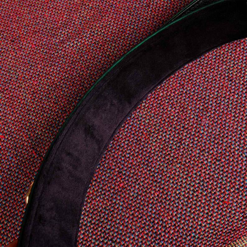May include: A close-up of a black and green fabric hat with a black velvet band. The hat is on a red and green patterned fabric.