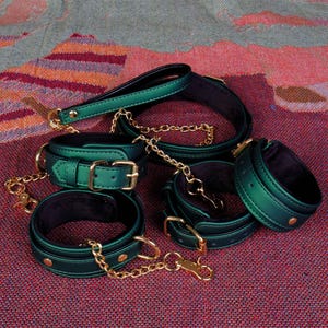 May include: A set of five green leather collars with gold hardware and chains. The collars are lined with black velvet and have a shiny, metallic finish.