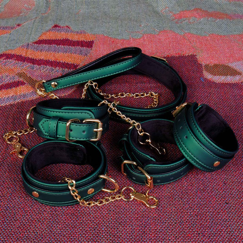 May include: A set of five green leather collars with gold hardware and chains. The collars are lined with black velvet and have a shiny, metallic finish.
