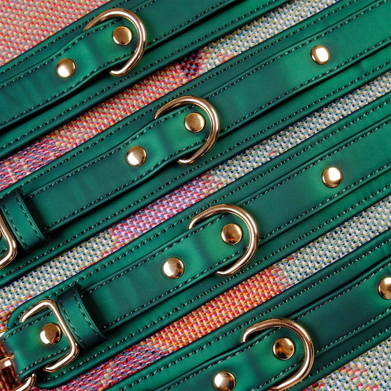 May include: Green leather straps with gold buckles and gold studs. The straps are arranged in a criss-cross pattern on a colorful fabric background.