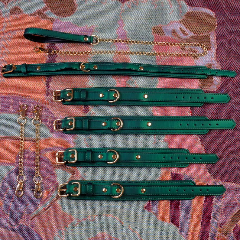 May include: Five green leather collars with gold hardware and two gold chains with clasps. The collars are arranged in a vertical stack on a patterned surface.