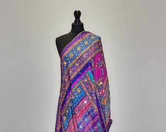 May include: A colourful shawl with a geometric pattern in shades of pink, blue, and purple. The shawl is decorated with gold embroidery and small mirrors.