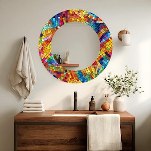 May include: A round mirror with a colorful mosaic tile design around the edge. The mosaic features a variety of colors including red, yellow, blue, and green. The mirror is mounted on a white wall above a wooden vanity.