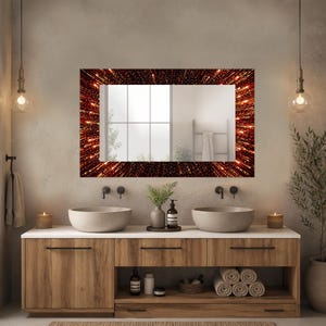 May include: A rectangular bathroom mirror with a dark red and gold starburst pattern frame. The mirror hangs above a wooden vanity with two vessel sinks and a white countertop. The bathroom has neutral-toned walls and decorative lighting.