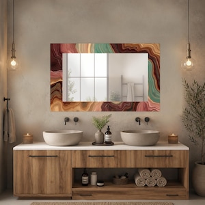 May include: A rectangular bathroom mirror with a colorful, agate-inspired border. The frame features bands of brown, red, green, and beige. The mirror is mounted above a wooden vanity with two vessel sinks and a white countertop.