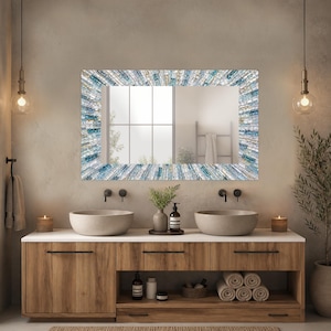 May include: A rectangular wall mirror featuring a decorative frame composed of numerous small, elongated glass tiles in shades of blue, white, and silver, arranged in a radial pattern that creates a textured, reflective surface around the glass.