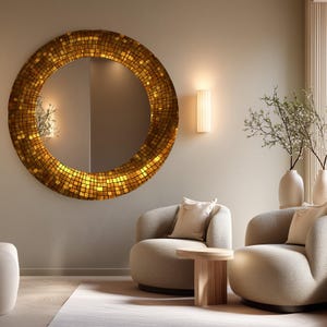 May include: A large, round mirror with a mosaic tile border in shades of gold and brown. The mirror is mounted on a neutral-colored wall, reflecting the room's interior. Two beige armchairs and a small wooden table are in front of the mirror.