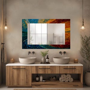 May include: A rectangular wall mirror featuring a decorative border with a mosaic pattern of small tiles in shades of deep blue, bright yellow, and fiery orange. The mirror reflects a bright room with a window and a towel rack on the wall.
