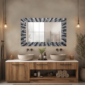 May include: A rectangular bathroom mirror with a mosaic-style frame in shades of black, white, and gray. The mirror is mounted above a wooden vanity with two vessel sinks and a white countertop. The room has a neutral color palette.