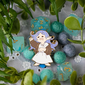 Könnte beinhalten: Ein farbenfroher Emaille-Pin mit einer Cartoonfigur mit lila Haaren und einer braunen Jacke. Umgeben von türkisfarbenen Würfeln, Filzkugeln und Grünzeug. Ein lustiges Accessoire für Fantasy-Spiele-Fans.
