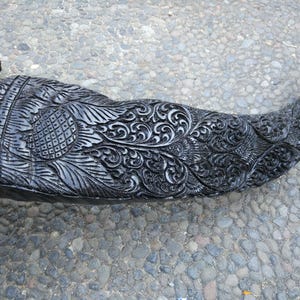 May include: A black carved horn with intricate floral designs. The horn is polished and has a smooth surface.
