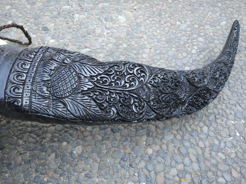 May include: A black carved horn with intricate floral designs. The horn is polished and has a smooth surface.