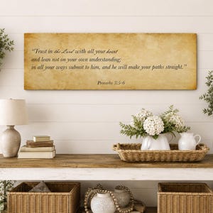 Op de afbeelding: Een rechthoekig wandbord met een beige, perkamentachtige achtergrond met de zwarte gedrukte tekst: "Trust in the Lord with all your heart and lean not on your own understanding; in all your ways submit to him, and he will make your paths straight." Proverbs 3:5-6.