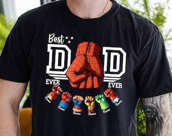 Könnte beinhalten: Schwarzes T-Shirt mit dem weißen Text "Best Dad Ever". Das Design umfasst eine große rote Faust und mehrere kleinere Fäuste in verschiedenen Farben. Das Shirt zeigt auch eine Auswahl an Faustdesigns.