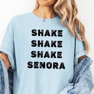 May include: A light blue t-shirt with the text "SHAKE SHAKE SHAKE SENORA" printed in black.