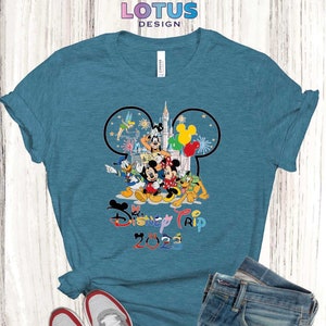 Puede incluir: Una camiseta azul turquesa con un gr&aacute;fico de Mickey Mouse y otros personajes de Disney frente al Castillo de Cenicienta. El texto "Disney Trip 2023" est&aacute; impreso debajo del gr&aacute;fico.