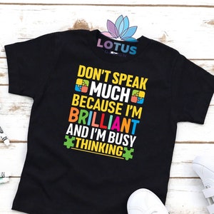 May include: Black t-shirt with a colorful graphic that says "Don't speak much because I'm brilliant and I'm busy thinking". The graphic features puzzle pieces.