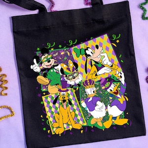 Puede incluir: Bolso tote negro con un dise&ntilde;o colorido de personajes de Disney con atuendos de Mardi Gras. Mickey, Minnie, Goofy, Pluto, Donald y Daisy Duck est&aacute;n representados. Serpentinas decorativas moradas, verdes y doradas rodean el bolso.