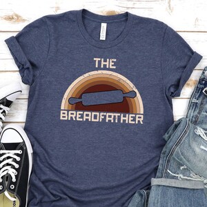 May include: A navy blue t-shirt with a vintage rainbow design and the text "The Breadfather" with a rolling pin graphic.