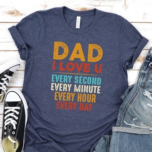 May include: A navy blue t-shirt with the text "DAD I LOVE U" in a retro font. The text is stacked vertically with the words "EVERY SECOND", "EVERY MINUTE", "EVERY HOUR", and "EVERY DAY" underneath.