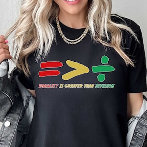 May include: Black t-shirt with a graphic of a red equals sign, a yellow greater than sign, and a green divided by sign. The text below the graphic reads "Equality is greater than division."