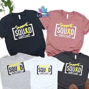 May include: Four t-shirts with the text "Support Squad" and a yellow ribbon. The shirts are in black, grey, white, and heather grey. The text "#MULTIPLEMYELOMACANCER" is below the ribbon.