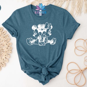 Pode incluir: Uma camiseta azul-petr&oacute;leo heather com um contorno branco do Mickey Mouse e da Minnie Mouse de m&atilde;os dadas. O texto "LOTUS DESIGN" est&aacute; impresso na camiseta.
