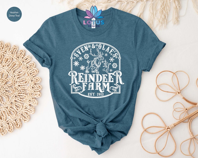 May include: A teal blue t-shirt with a white graphic design featuring a reindeer and the text "Sven & Olaf's Reindeer Farm Est. 2013".