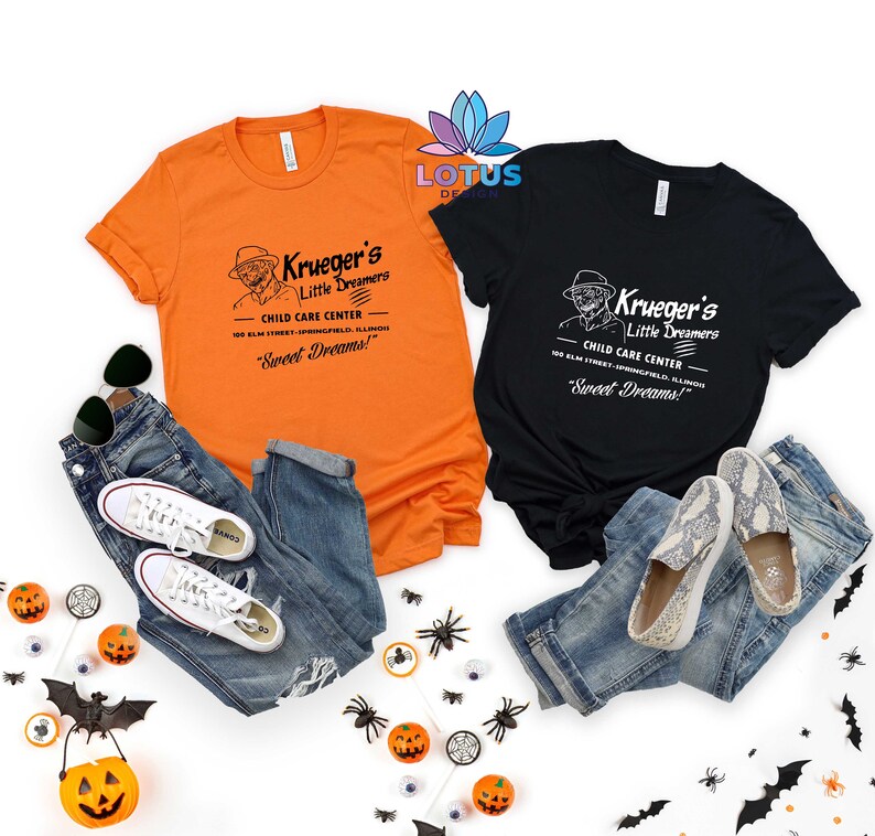 May include: Two t-shirts with a vintage-style graphic of a child care center called "Krueger's Little Dreamers". The text on the shirts reads "Child Care Center" and "Sweet Dreams!" The shirts are orange and black and are laid out on a white background with Halloween decorations.