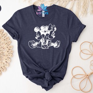 Pode incluir: Uma camiseta azul marinho heather com um gr&aacute;fico branco do Mickey Mouse e da Minnie Mouse sentados juntos. O gr&aacute;fico &eacute; um estilo de desenho de linha simples.
