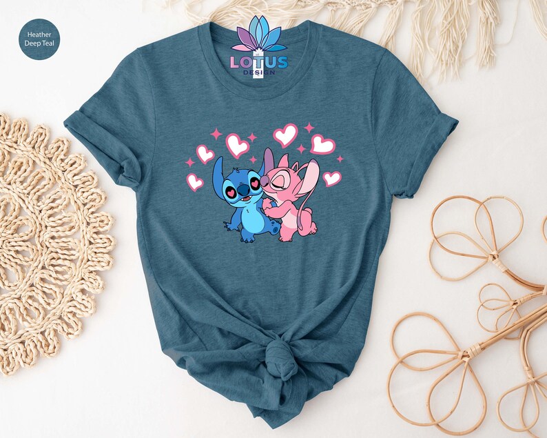 K&ouml;nnte beinhalten: Ein blaues T-Shirt mit einem Motiv von Stitch und Angel aus Lilo & Stitch. Das Motiv zeigt Stitch und Angel, die sich umarmen, mit Herzen und Glitzer um sie herum. Der Text "LOTUS DESIGN" ist auf das Shirt gedruckt.