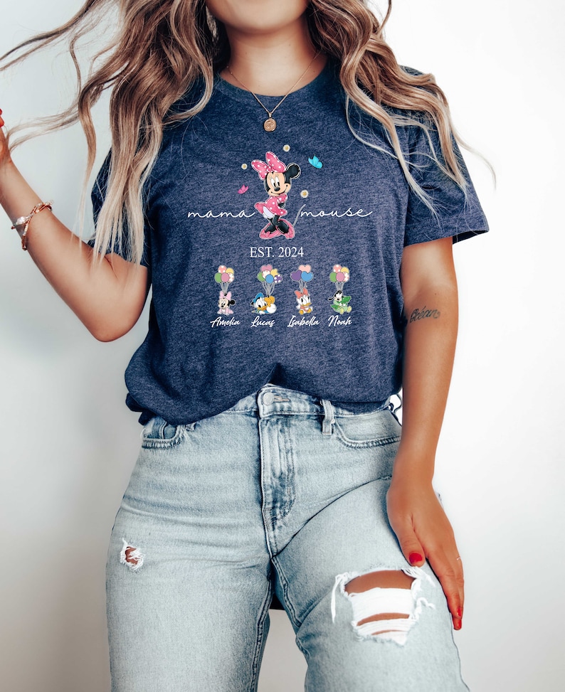 Puede incluir: Una camiseta azul marino con el texto "mama mouse est. 2024" y una imagen de dibujos animados de Minnie Mouse. Debajo de Minnie Mouse hay cuatro im&aacute;genes de dibujos animados de Mickey Mouse con los nombres "Amelia, Lucas, Isabella, Noah" impresos debajo de cada imagen.