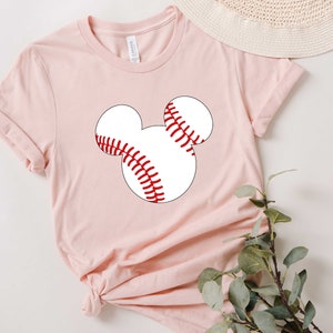 May include: A pink t-shirt with a white baseball graphic in the shape of Mickey Mouse's head.