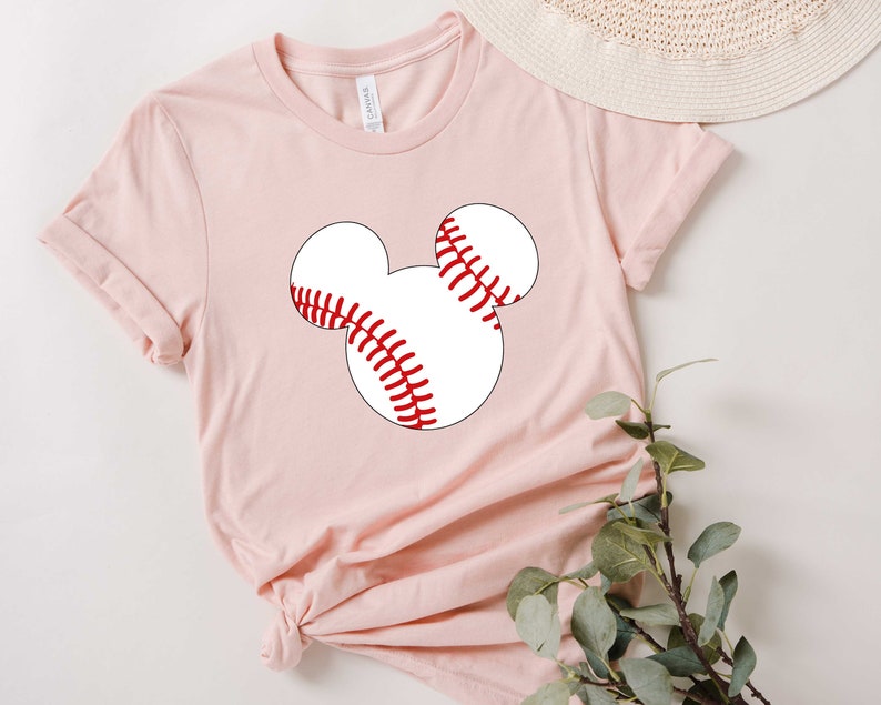 May include: A pink t-shirt with a white baseball graphic in the shape of Mickey Mouse's head.