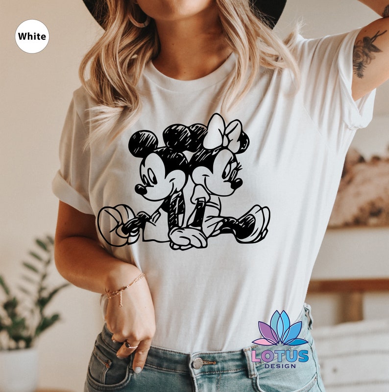Pode incluir: Camiseta branca com uma ilustra&ccedil;&atilde;o em preto e branco do Mickey Mouse e da Minnie Mouse de m&atilde;os dadas. A ilustra&ccedil;&atilde;o &eacute; em estilo de esbo&ccedil;o.