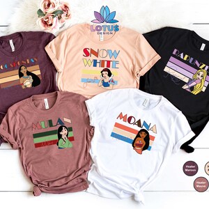 May include: Five different t-shirts featuring Disney princesses with retro-style graphics. The shirts are in various colours, including maroon, peach, white, and black. Each shirt features a different princess, including Pocahontas, Snow White, Rapunzel, Mulan, and Moana.
